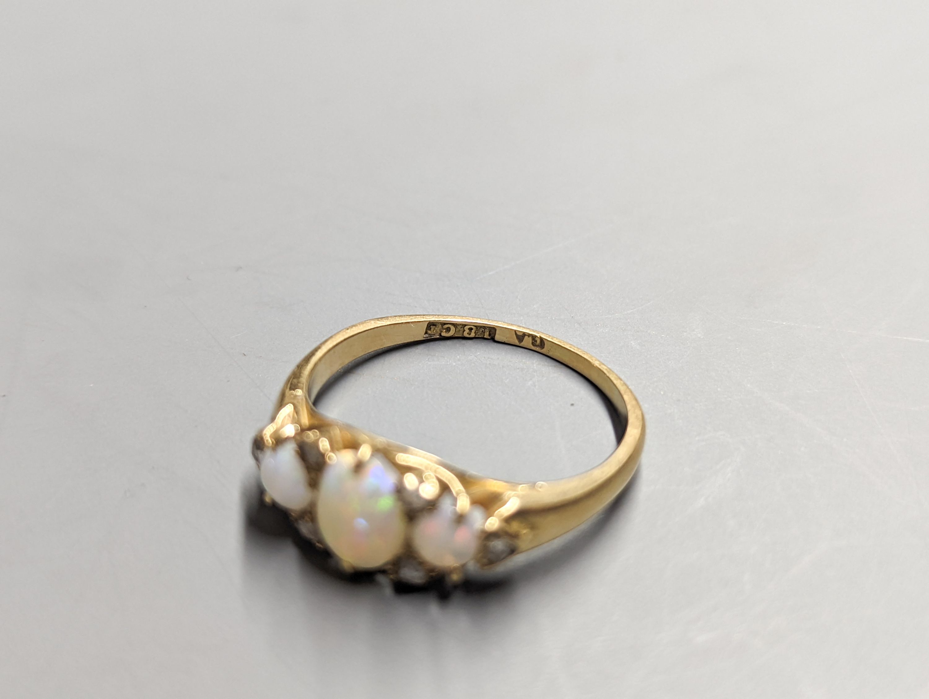 An early 20th century 18ct and three stone white opal set ring, with diamond chip spacers, size Q/R, gross 3.7 grams.